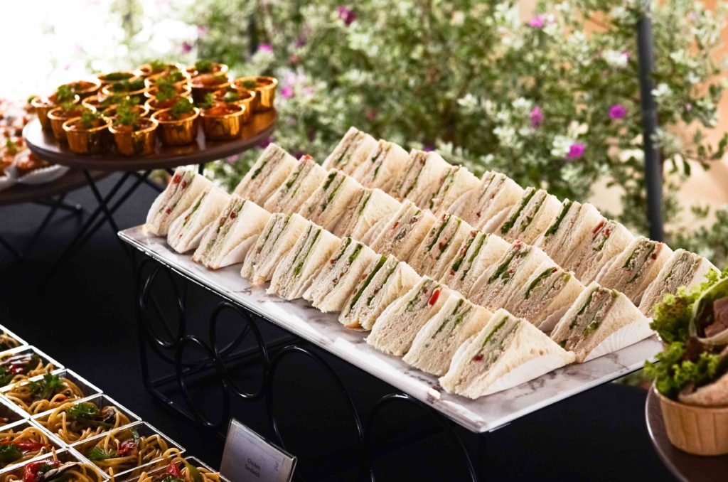 Finger sandwiches lined on a marble board beside gold-cup bites at an iDoCatering launch event