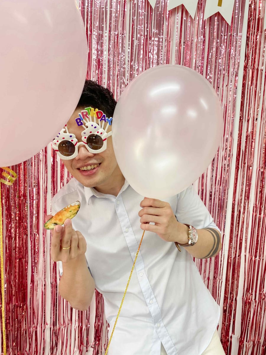 Guest in novelty birthday glasses holding a baked snack between balloons, birthday party catering 2022