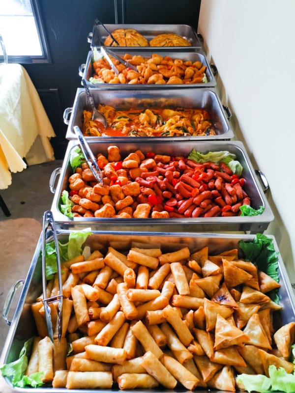 Chafing dishes of spring rolls, samosas, chicken nuggets, cocktail sausages and curry on an iDoCatering buffet line