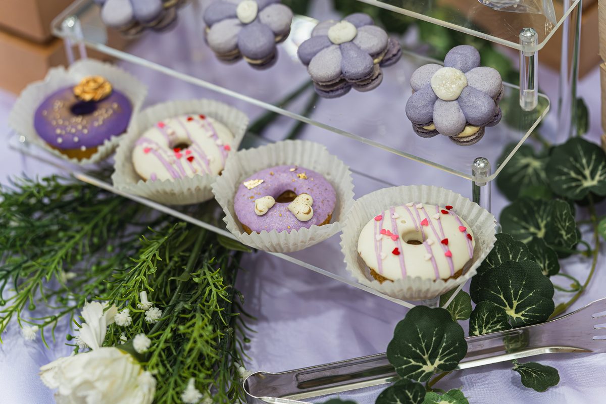 Party dessert display of glazed donuts, flower macarons and cake pops on acrylic tiers — iDoCatering