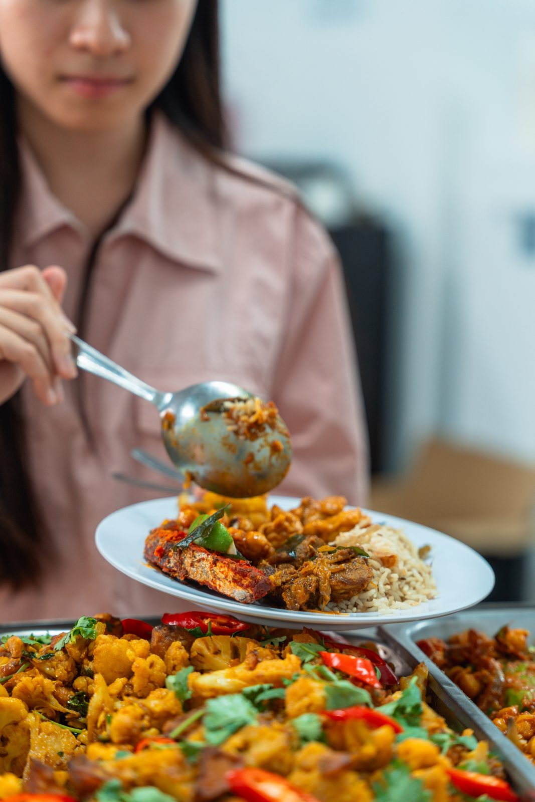Plate of masala fried fish, chicken curry and briyani rice served over a tray of aloo gobi at a Deepavali buffet