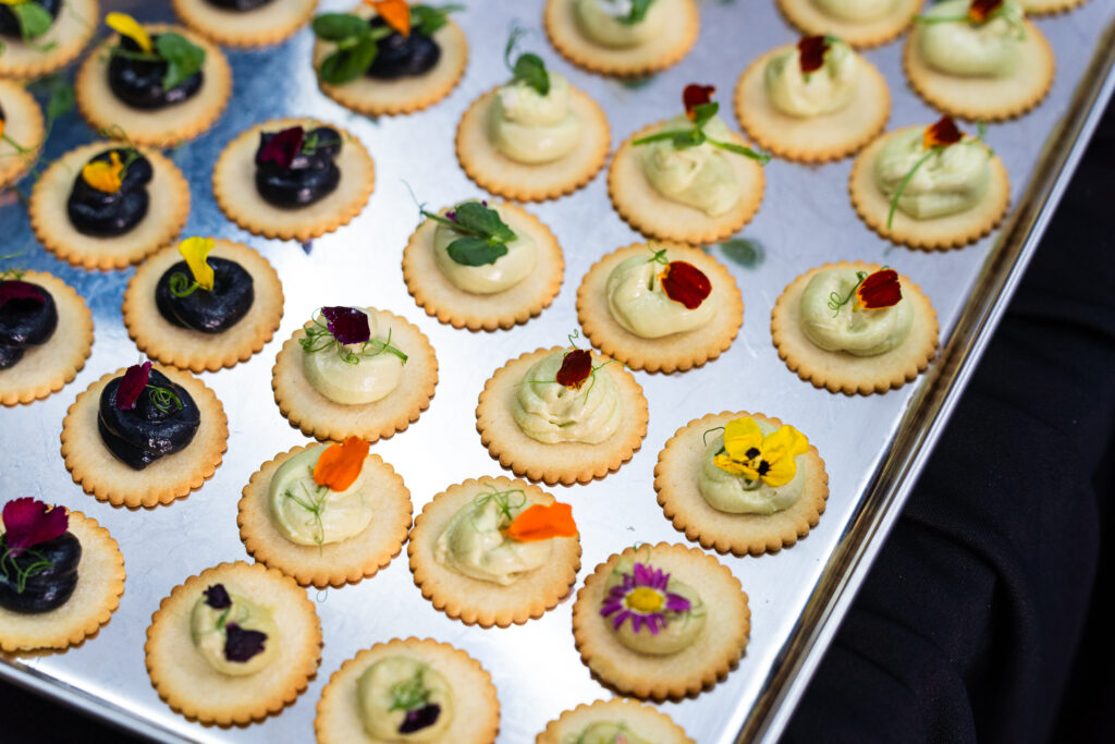 Squid ink and avocado cream canapés topped with edible flowers on a silver tray - iDoCatering