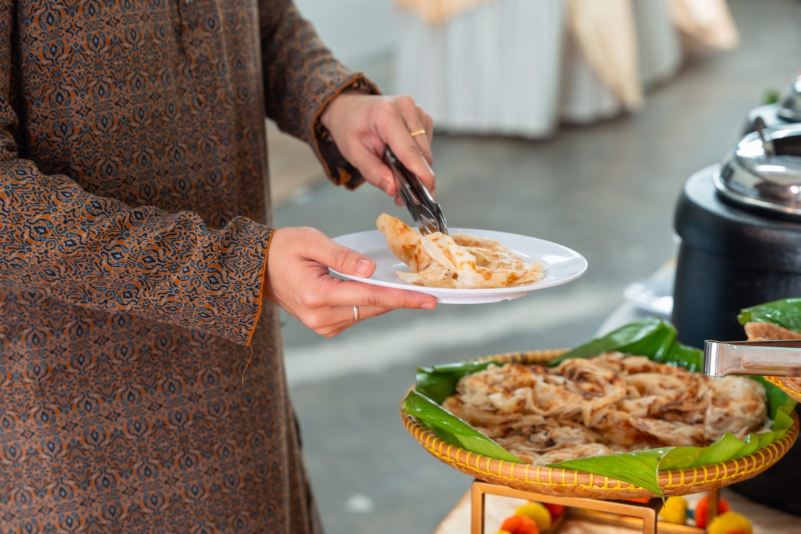 Guest in batik serving flaky roti canai from a rattan basket lined with banana leaf at an iDoCatering Deepavali buffet