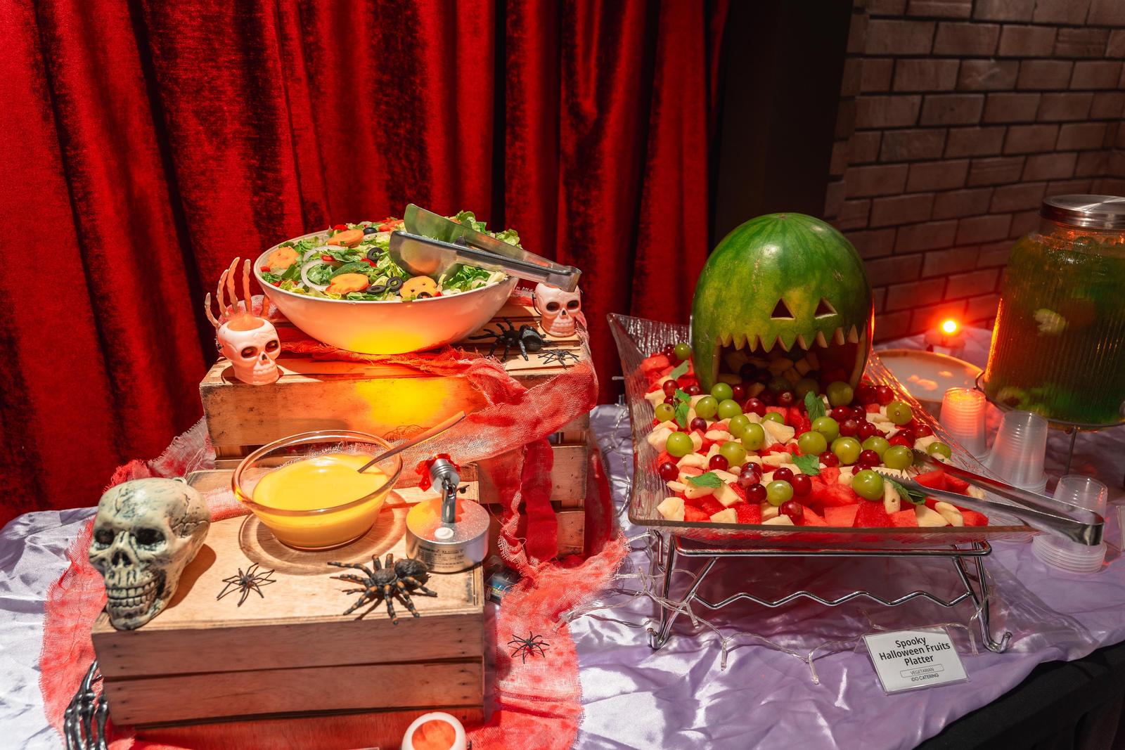 Halloween buffet with a carved watermelon fruit platter, salad and skull decor at an iDoCatering party