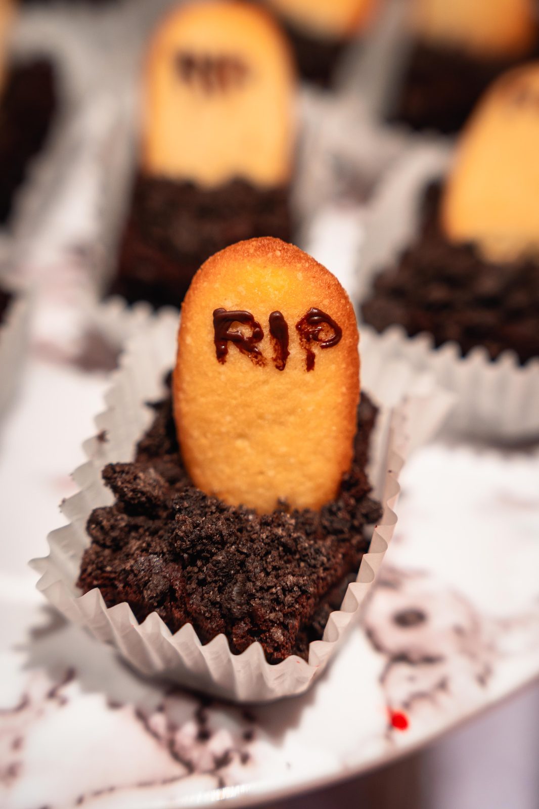 Single Graveyard Brownie cup with a RIP sponge tombstone in cookie-crumb soil, iDoCatering Halloween dessert