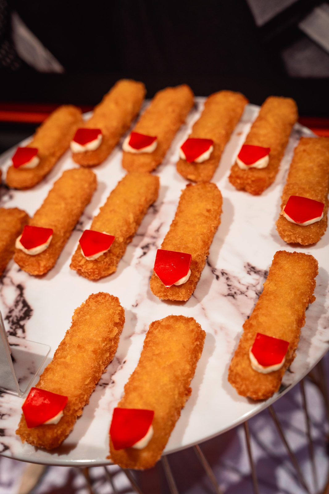 Witch Finger seafood sticks with red jelly nails arranged on a marble platter at a Halloween party buffet