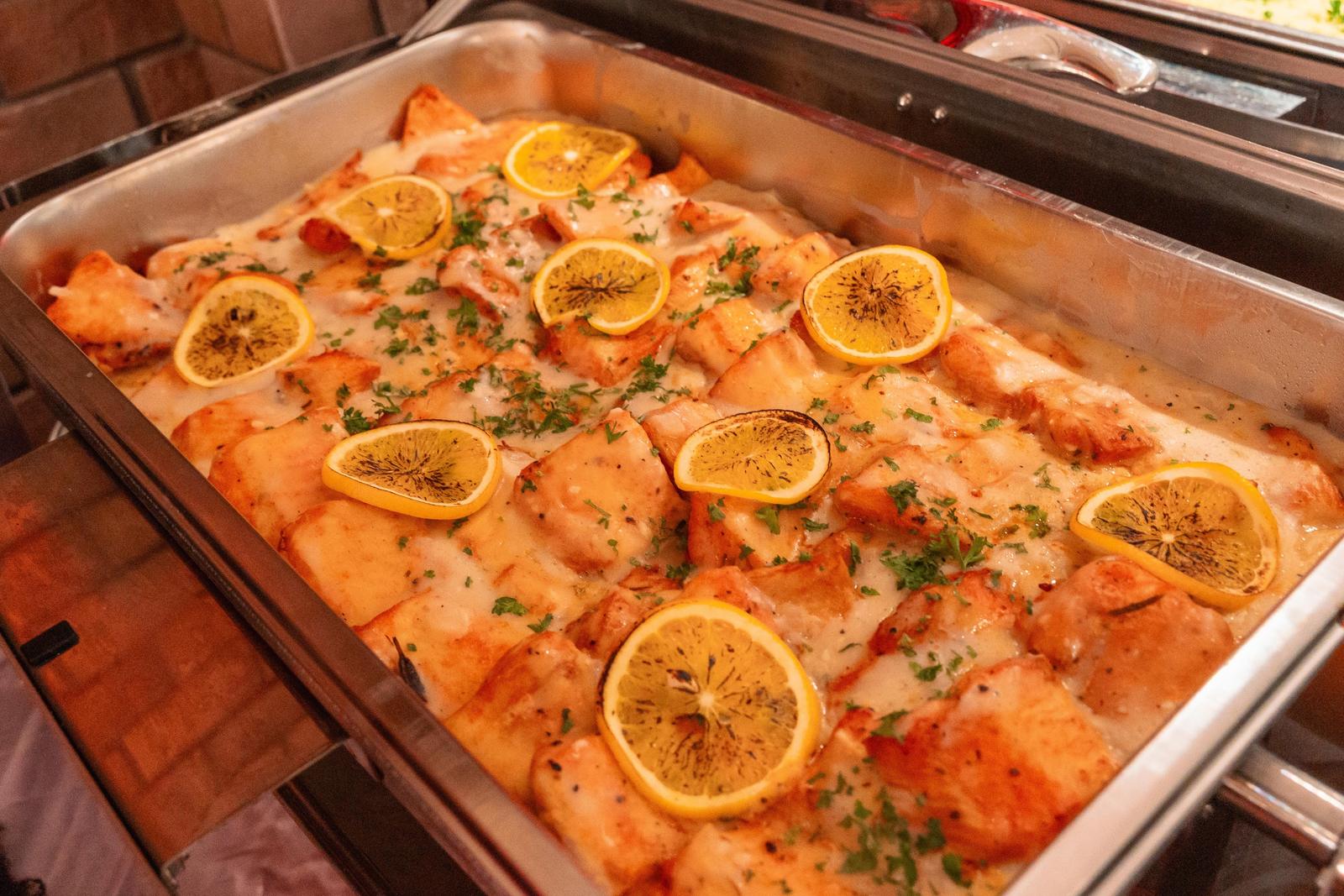 Baked fish fillet in cream sauce topped with orange slices and parsley in a chafing tray at a Halloween buffet