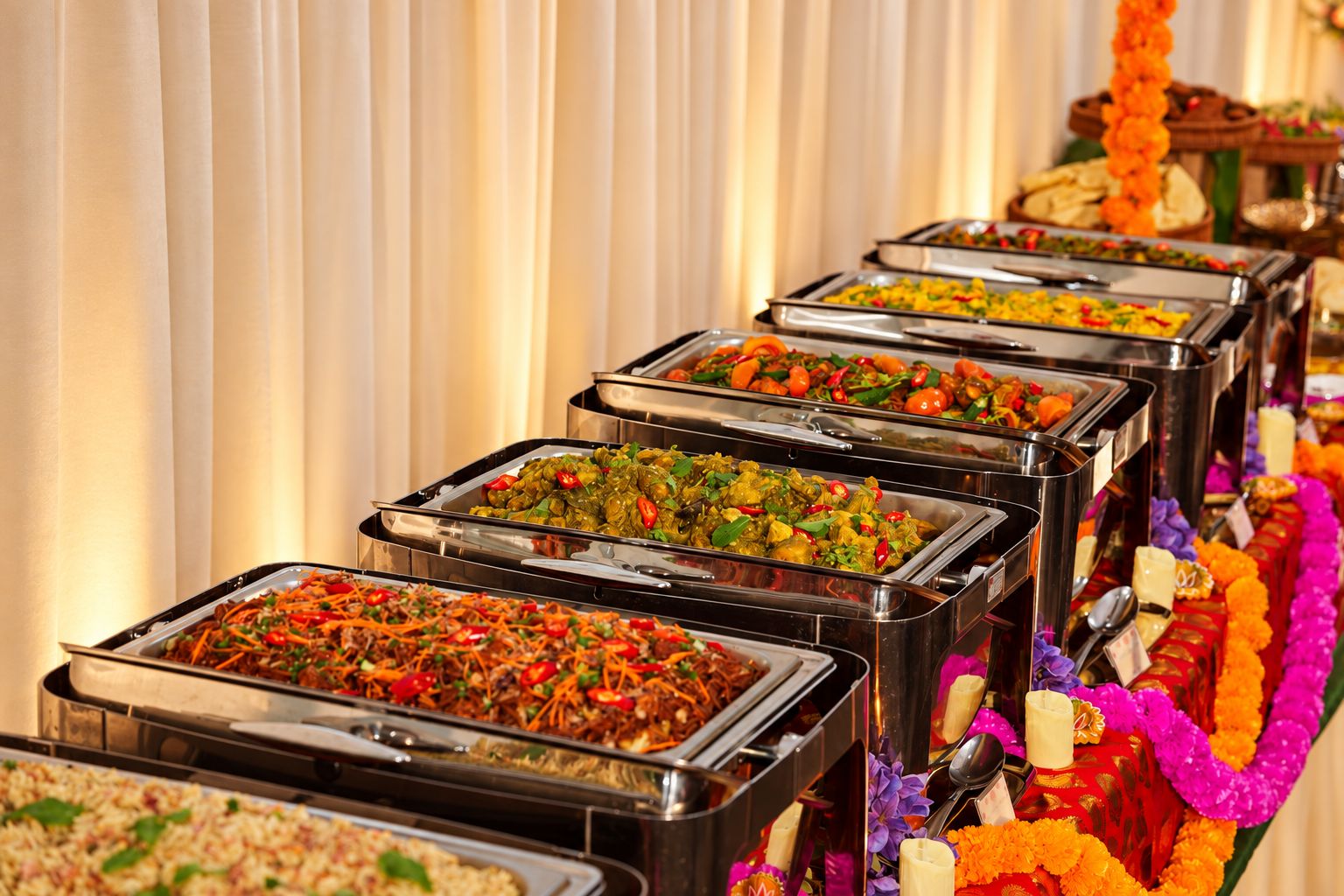 iDoCatering Deepavali buffet line of mee goreng and vegetable curries in chafing dishes beside marigold garlands