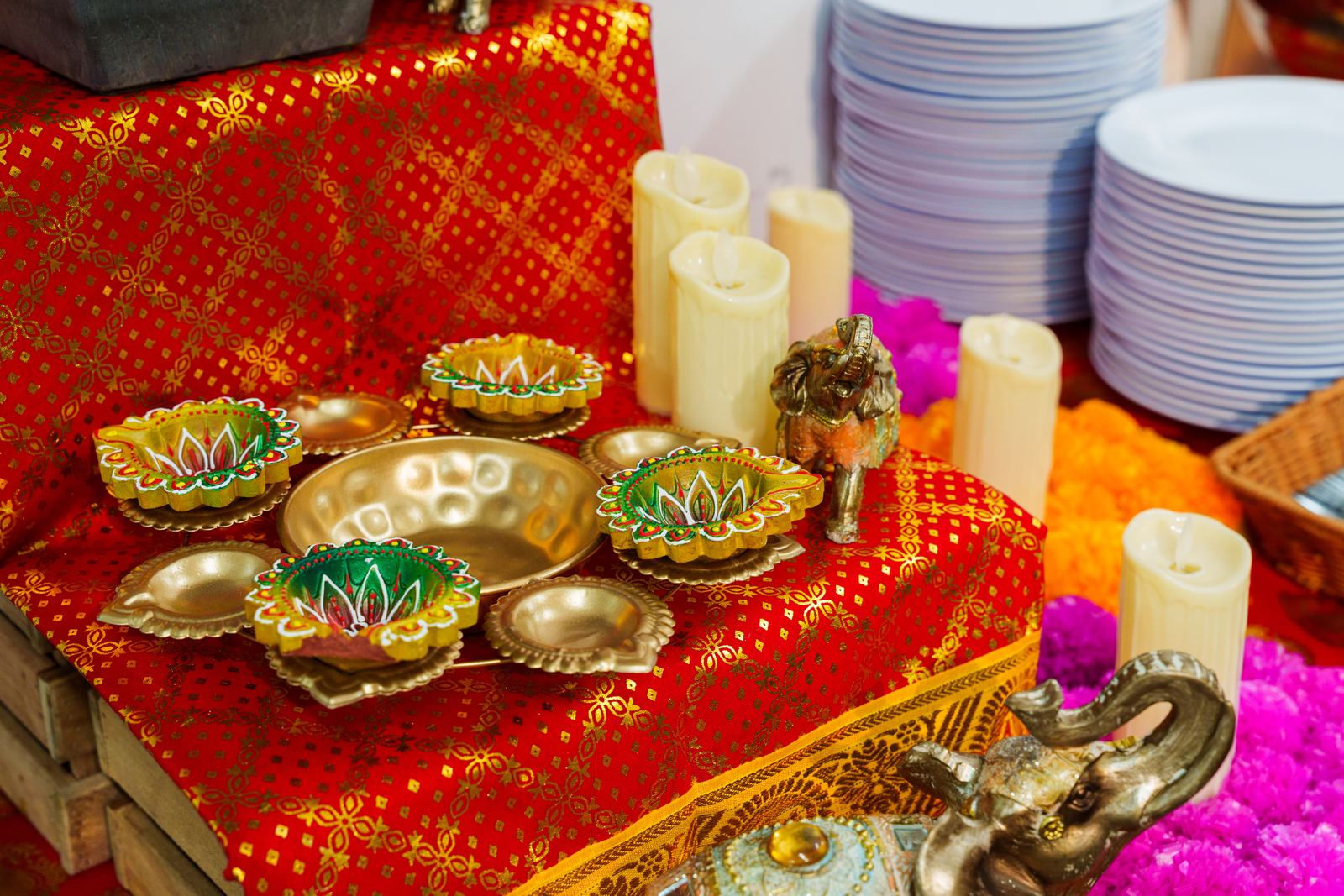 Painted diya oil lamps and brass dishes on red and gold sari cloth beside a brass elephant at a Deepavali buffet