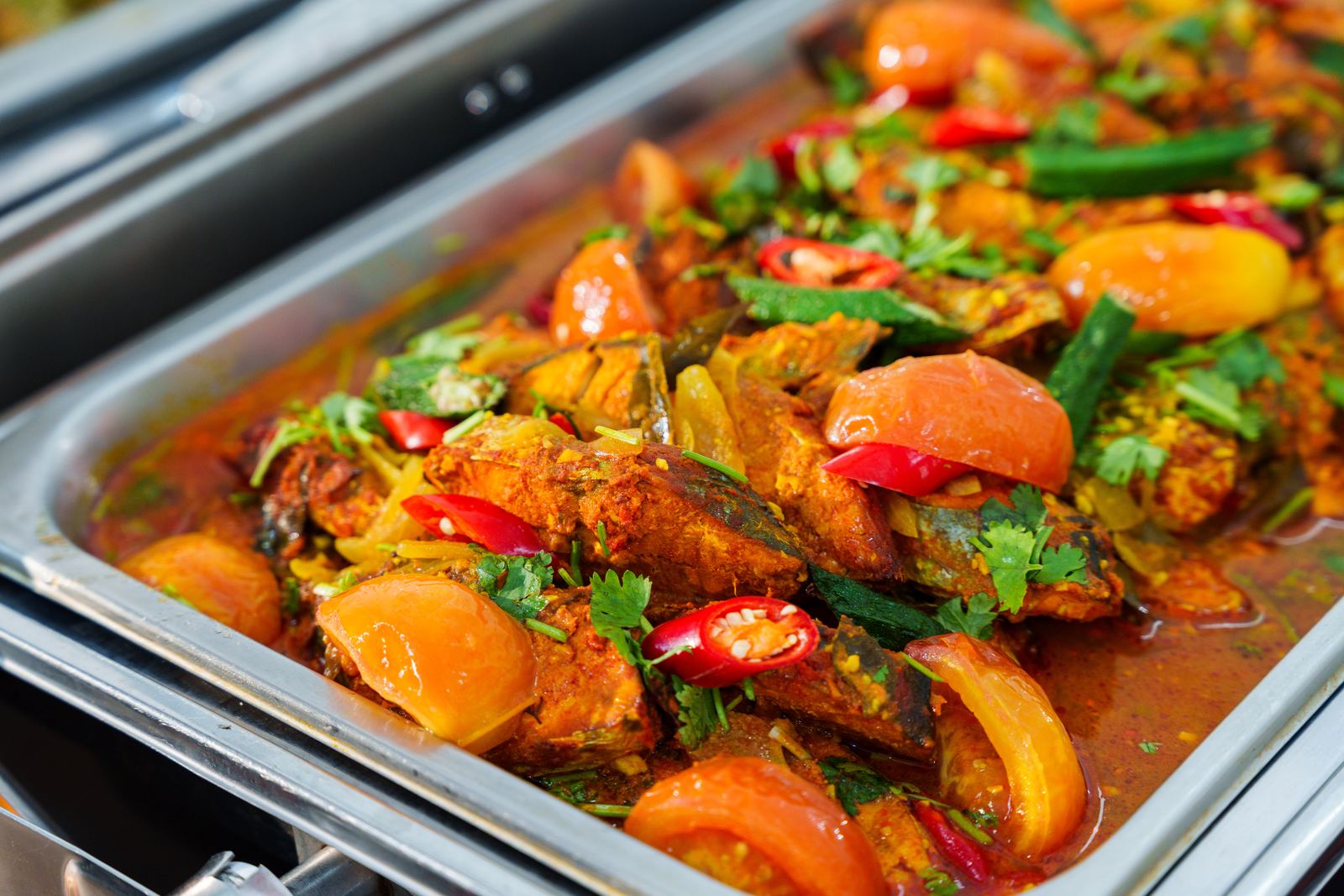 Fish curry with okra, tomato wedges and red chilli in a chafing dish at an iDoCatering Deepavali buffet