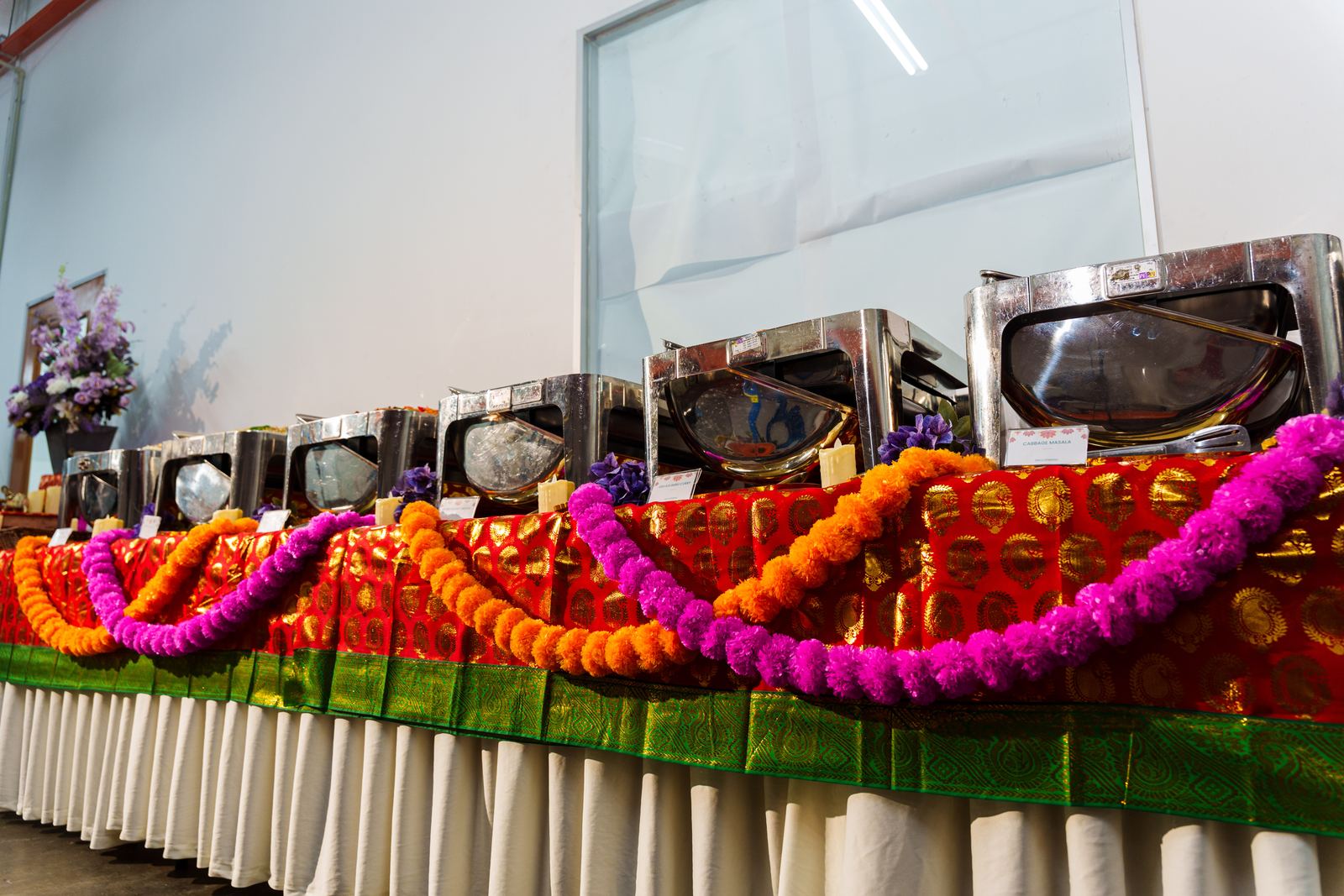 Deepavali buffet line of chafing dishes on red and gold sari cloth draped with marigold garlands