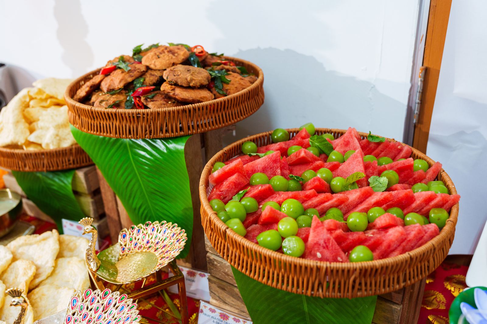 Rattan baskets of vadai, watermelon and grape fruit platter and papadom at a Deepavali buffet