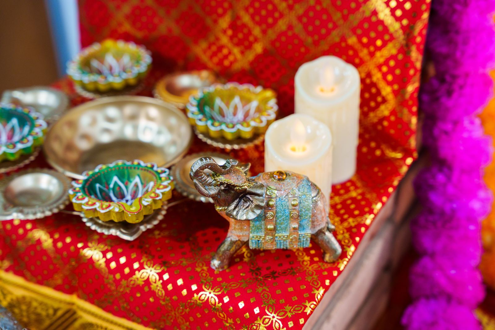 Painted lotus diya lamps, silver bowls and a brass elephant on red and gold sari cloth at Deepavali