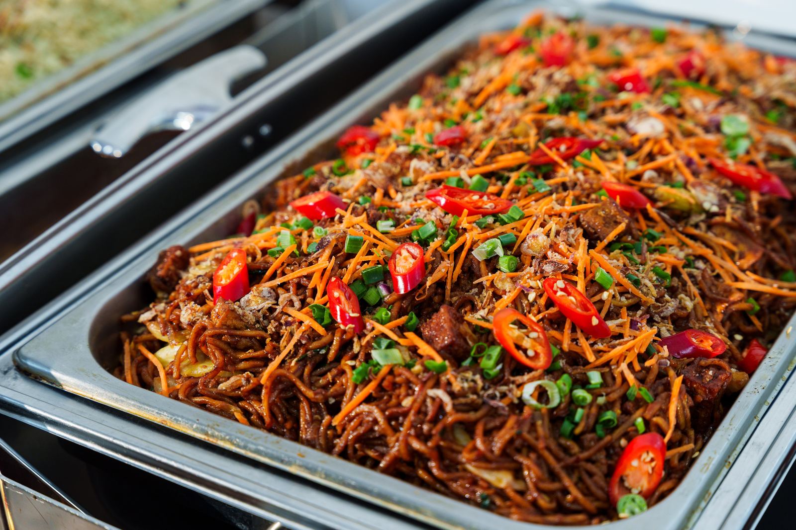 Mee goreng topped with shredded carrot, spring onion and red chilli in a chafing dish