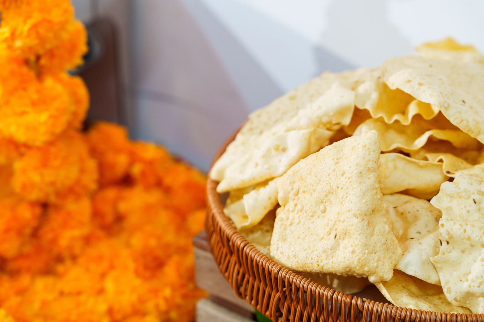 Basket of crisp papadom beside a marigold garland at an iDoCatering Deepavali buffet