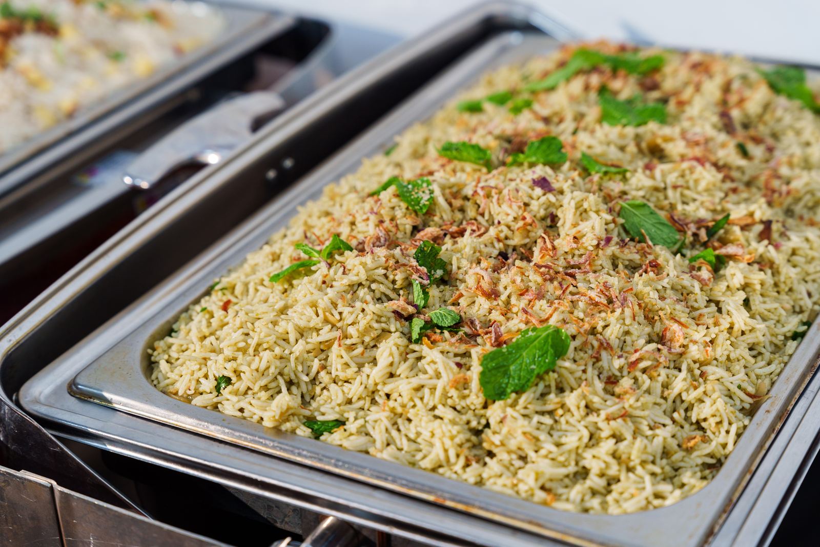 Pudina mint rice topped with mint leaves and fried shallots in a chafing dish at a Deepavali buffet