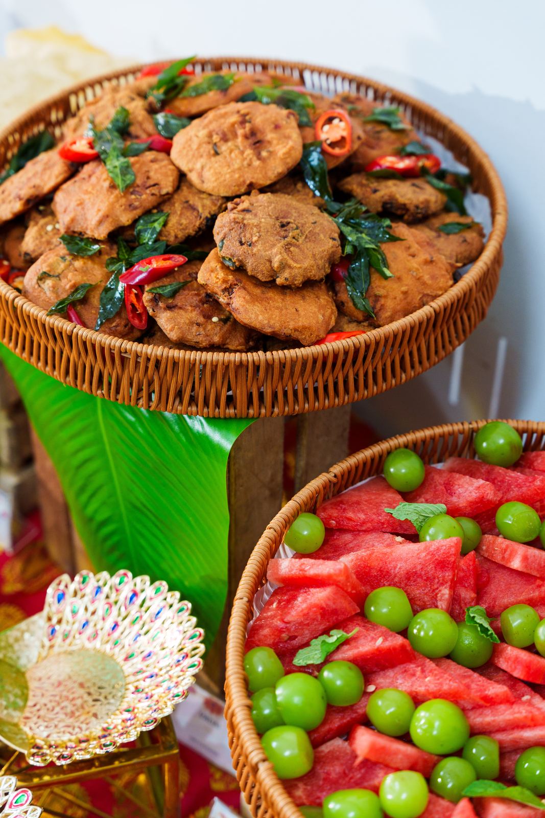 Rattan basket of vadai with curry leaves above a watermelon and grape fruit platter at Deepavali
