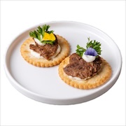 Shredded steak with cream and parsley on two crisp crackers, on a white plate — iDoCatering canapé