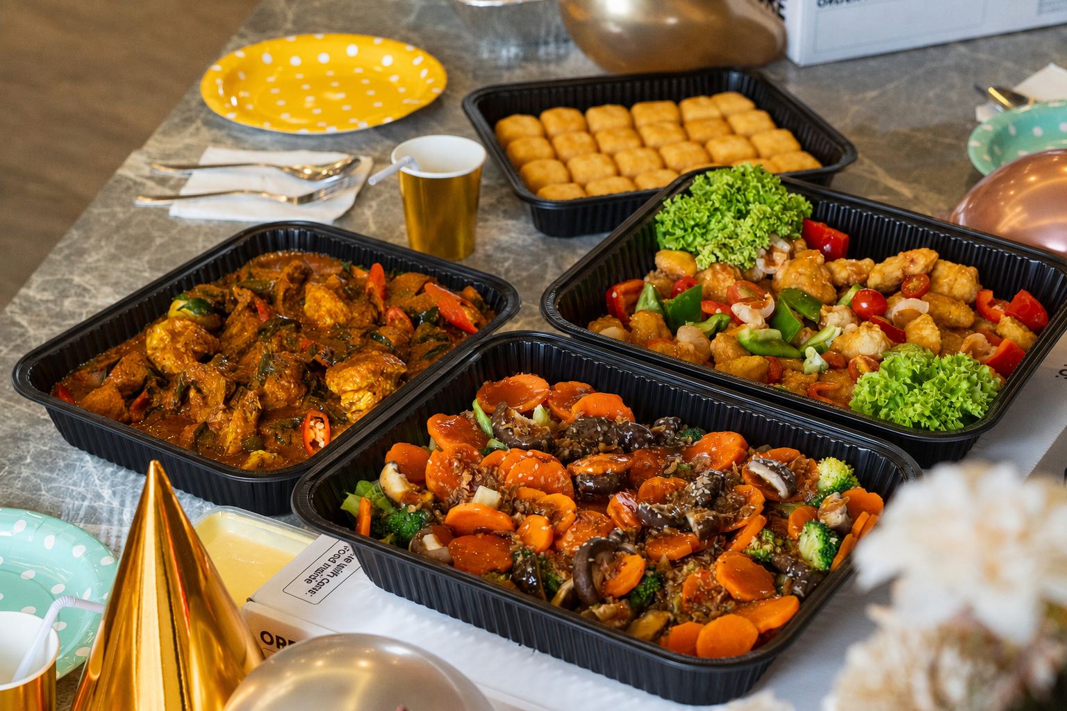 Four black catering trays of curry chicken, sweet and sour chicken, mushroom vegetable stir-fry and golden buns
