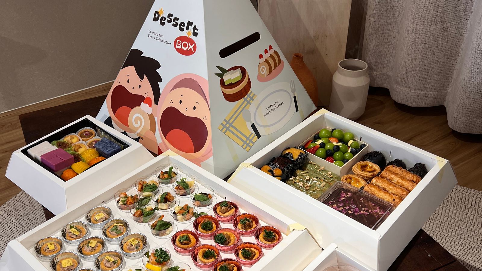 iDoCatering Pyramid Dessert Box — branded pyramid carton beside open trays of canapes, Nyonya kuih, pastries and trifle cups