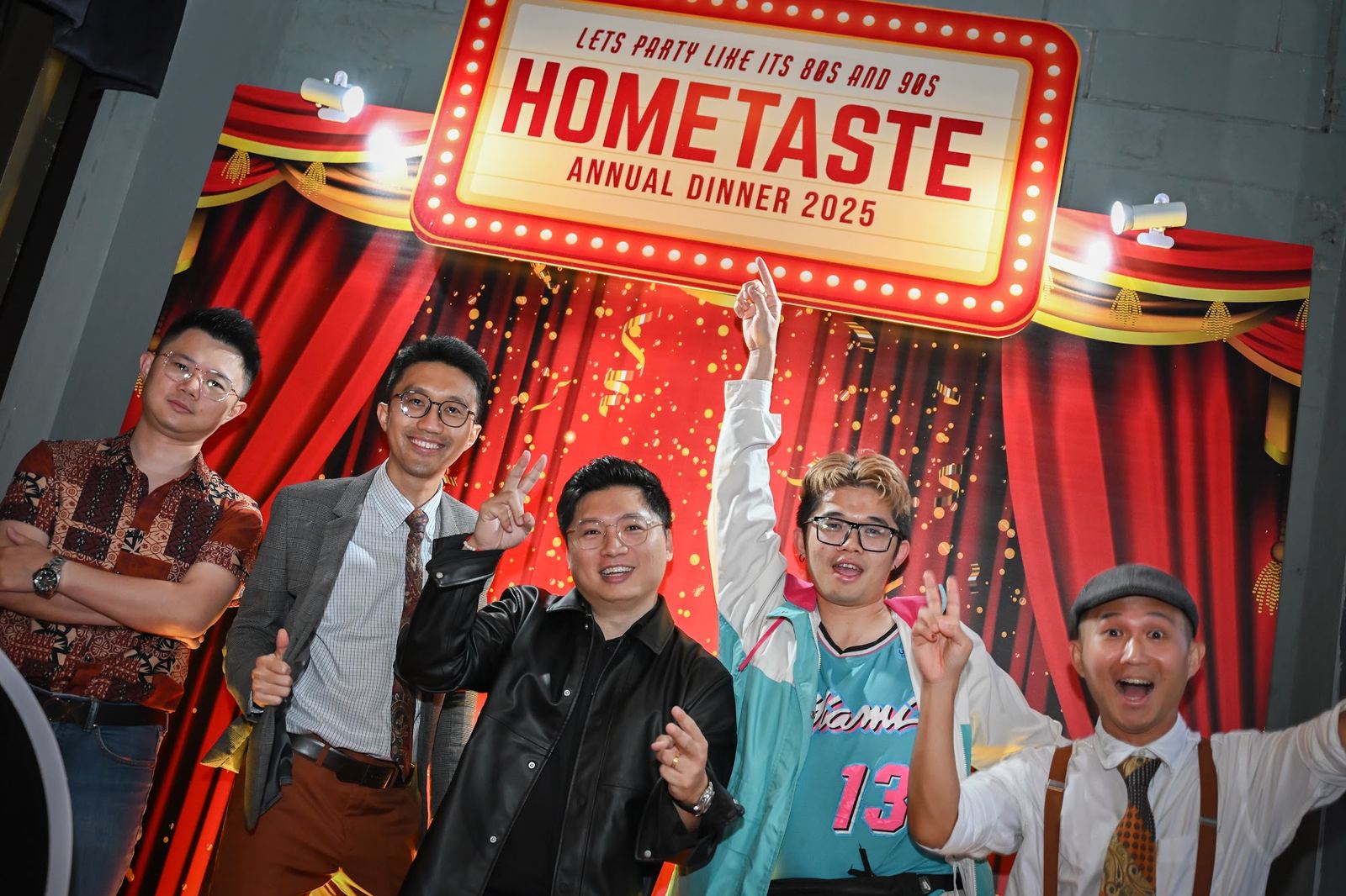 Five colleagues cheering in retro dress in front of the Hometaste annual dinner 2025 marquee backdrop