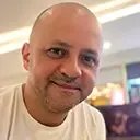 Smiling man with short hair indoors wearing a beige shirt.