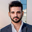 Portrait of a man with dark hair, beard, and mustache wearing a dark blazer and white shirt.