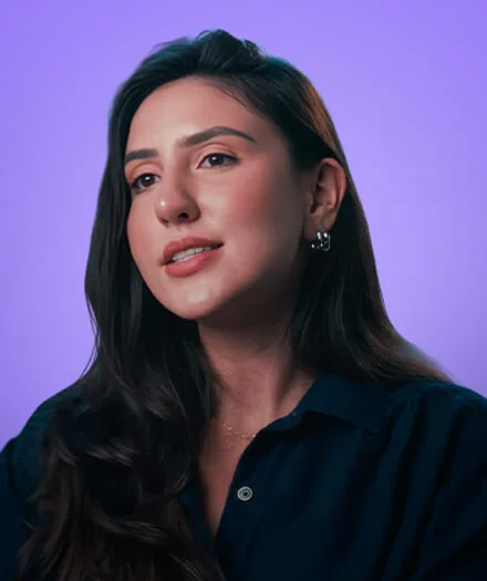 Portrait of a woman with long dark hair and hoop earrings against a purple background.