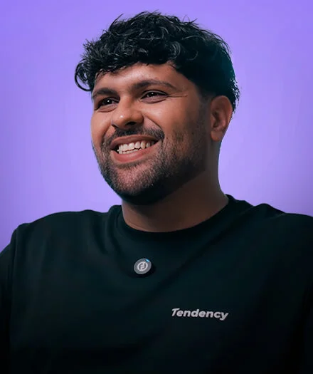 Smiling man with curly hair in a black shirt with 'Tendency' text on a purple background.