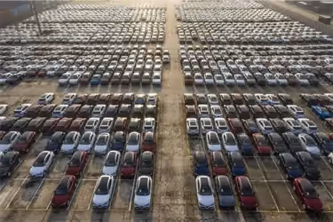Aerial view of thousands of new cars parked in tight rows at a massive shipping port parking lot.
