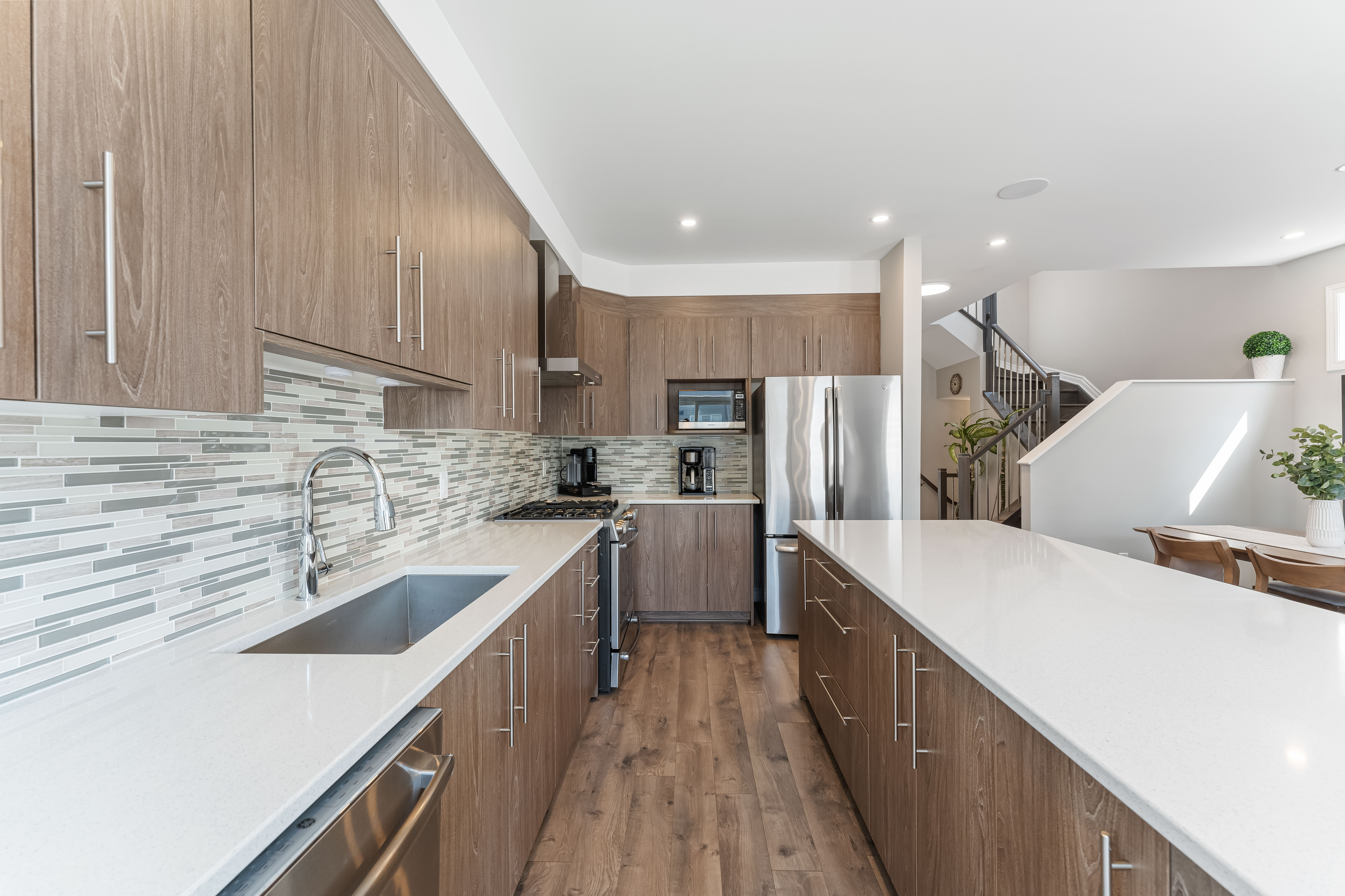 A kitchen with a long counter, stainless appliances and a staircase beyond