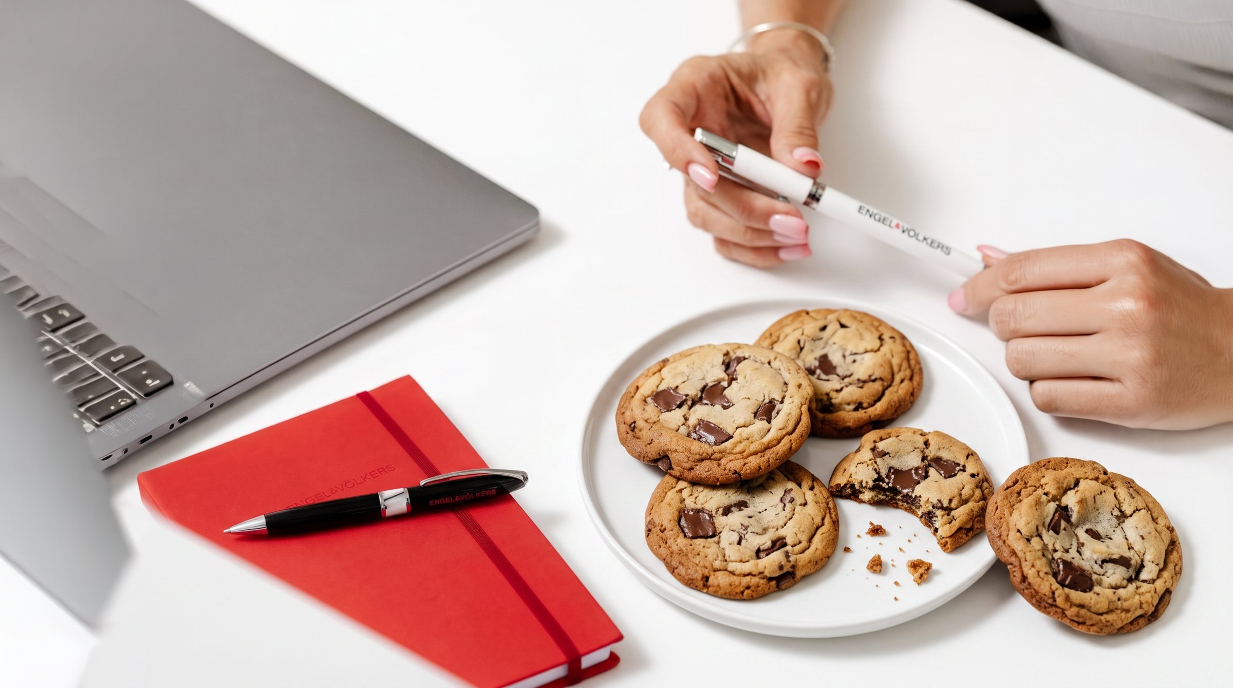 A plate of cookies beside an Engel & Völkers notebook and pen on a meeting table