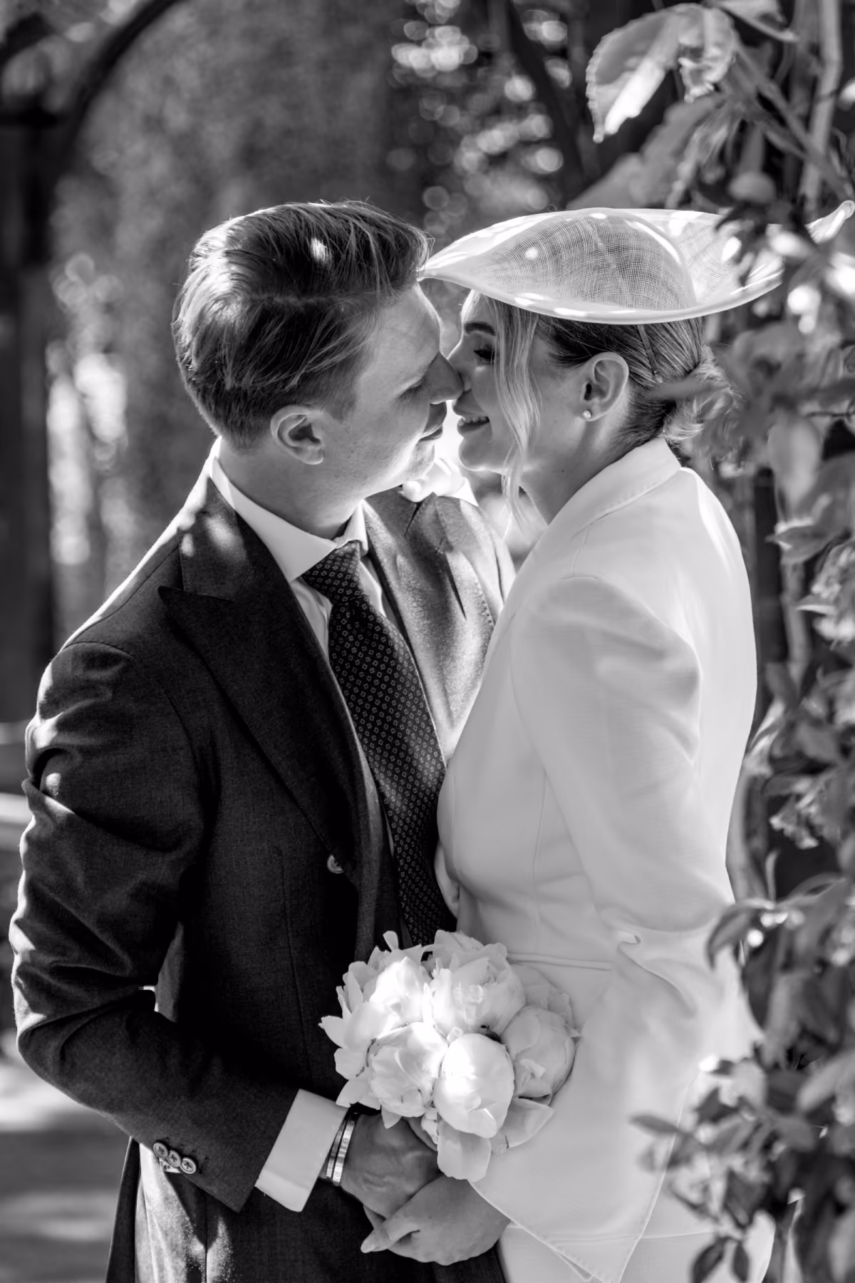 Black and white photo of a couple touching noses, with the woman holding a bouquet of flowers.