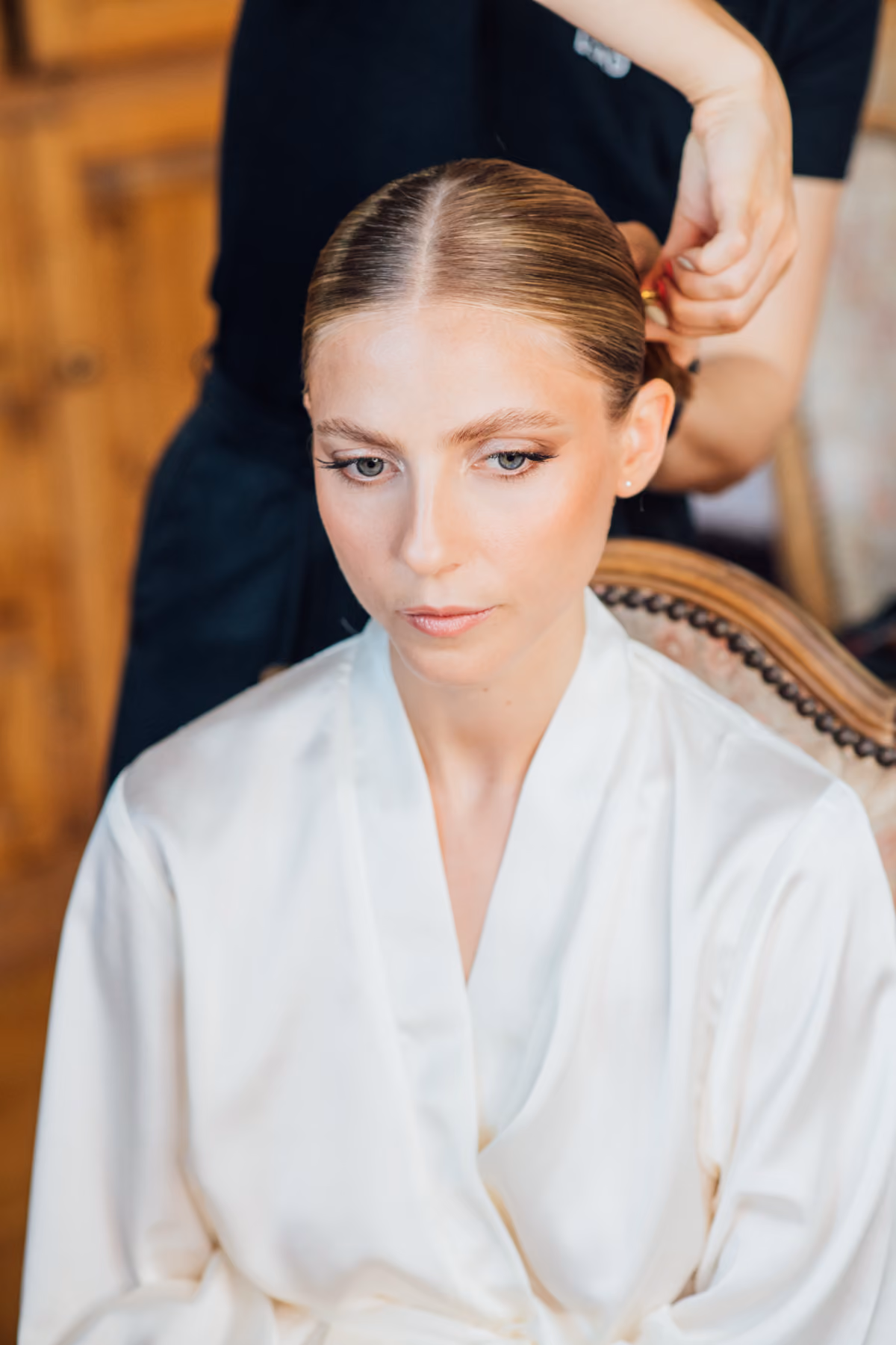 Woman with sleek hair in a white robe having her hair styled by another person.