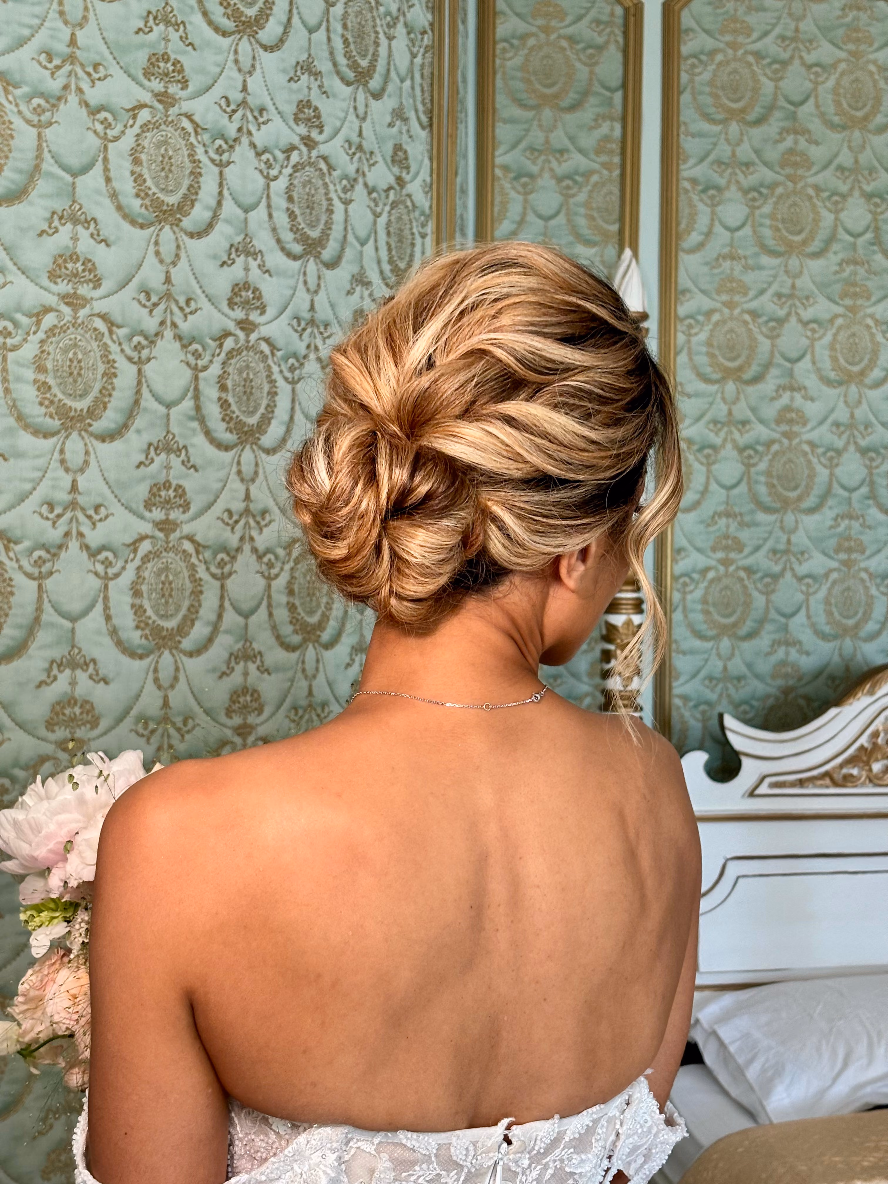 Woman with blonde hair styled in an elegant low bun wearing a white lace dress.