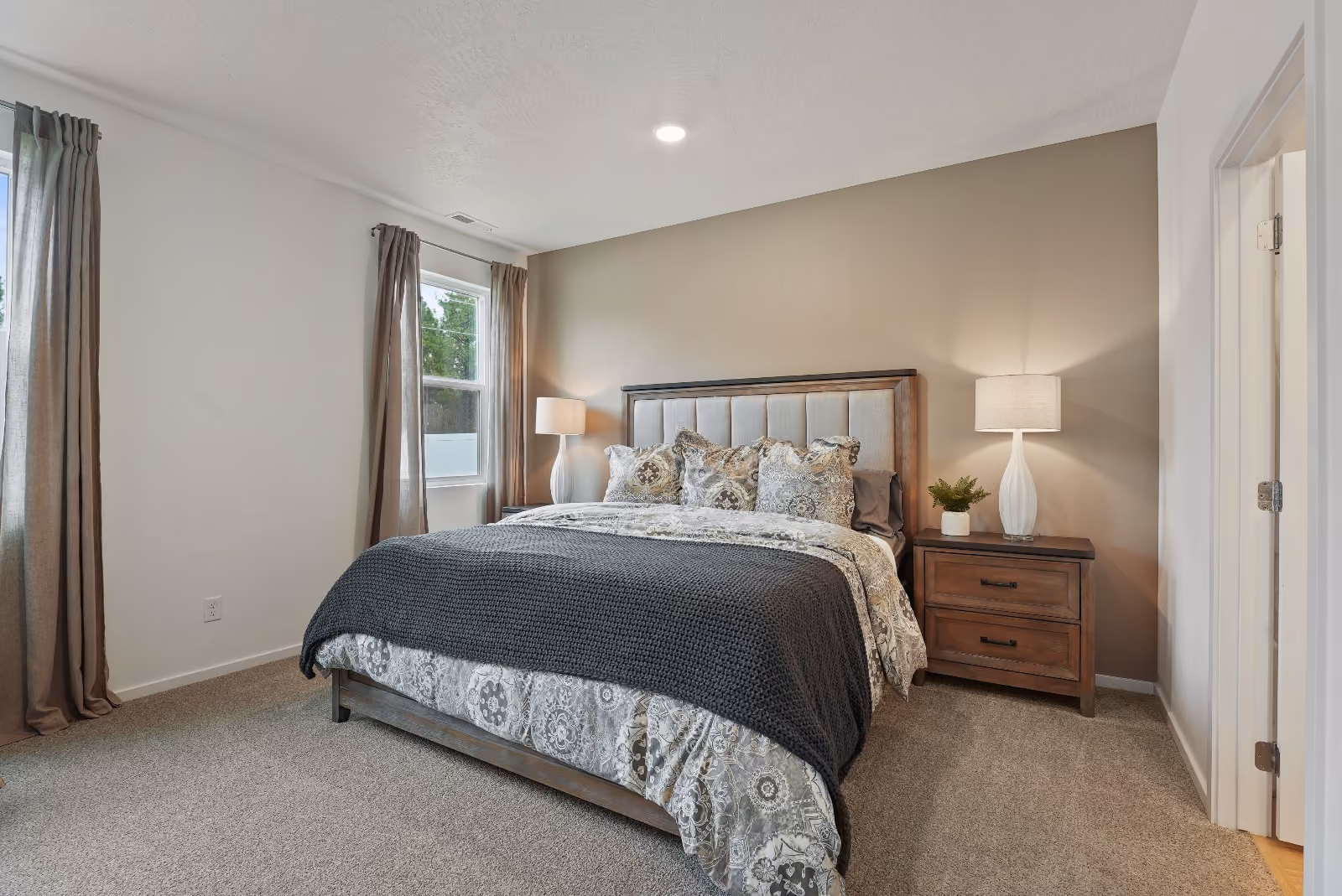 The primary bedroom: carpeted, with two windows, a warm greige accent wall, and a door through to the bath.