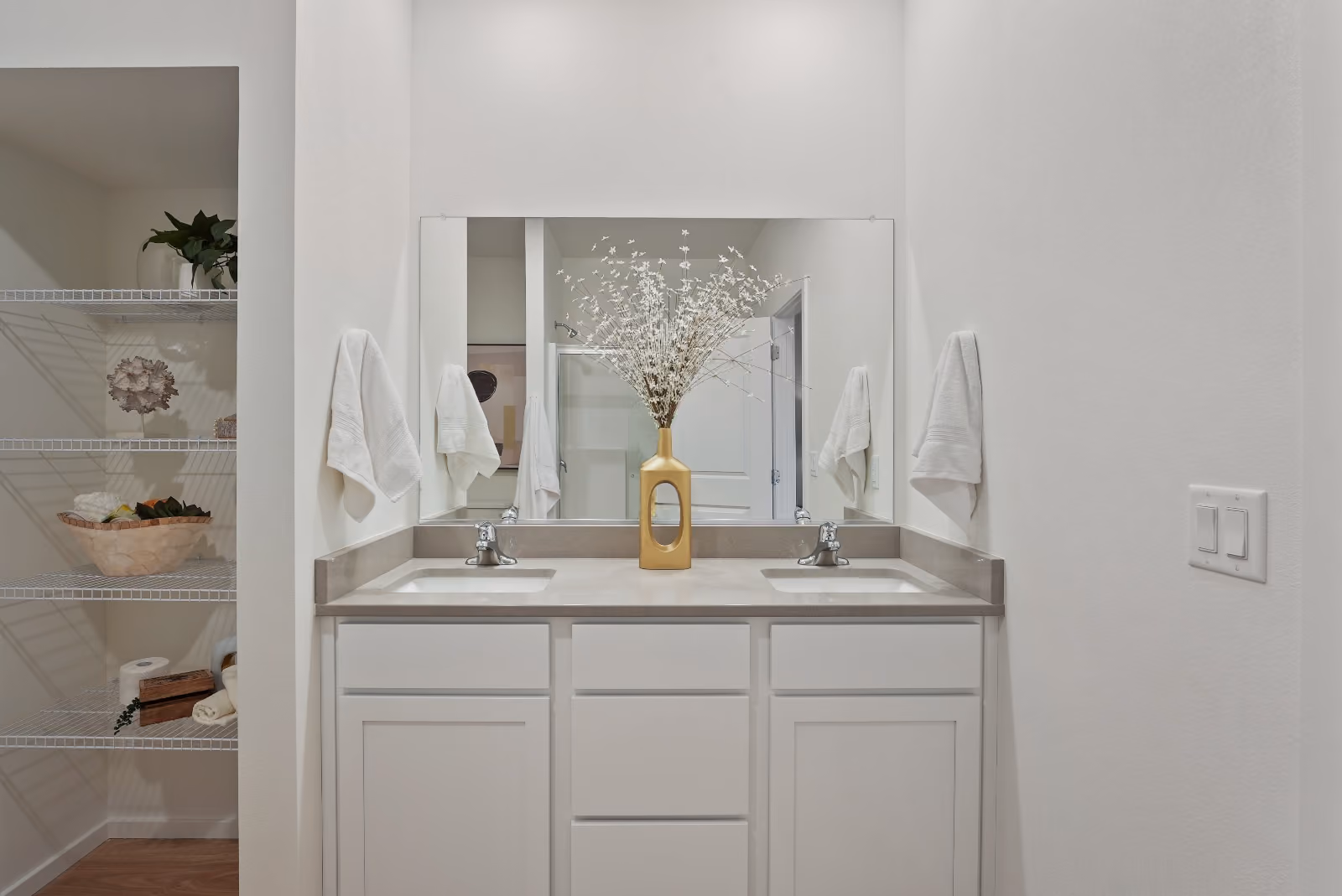 The primary bath with a dual-sink quartz vanity, wide mirror, and a walk-in closet alongside.