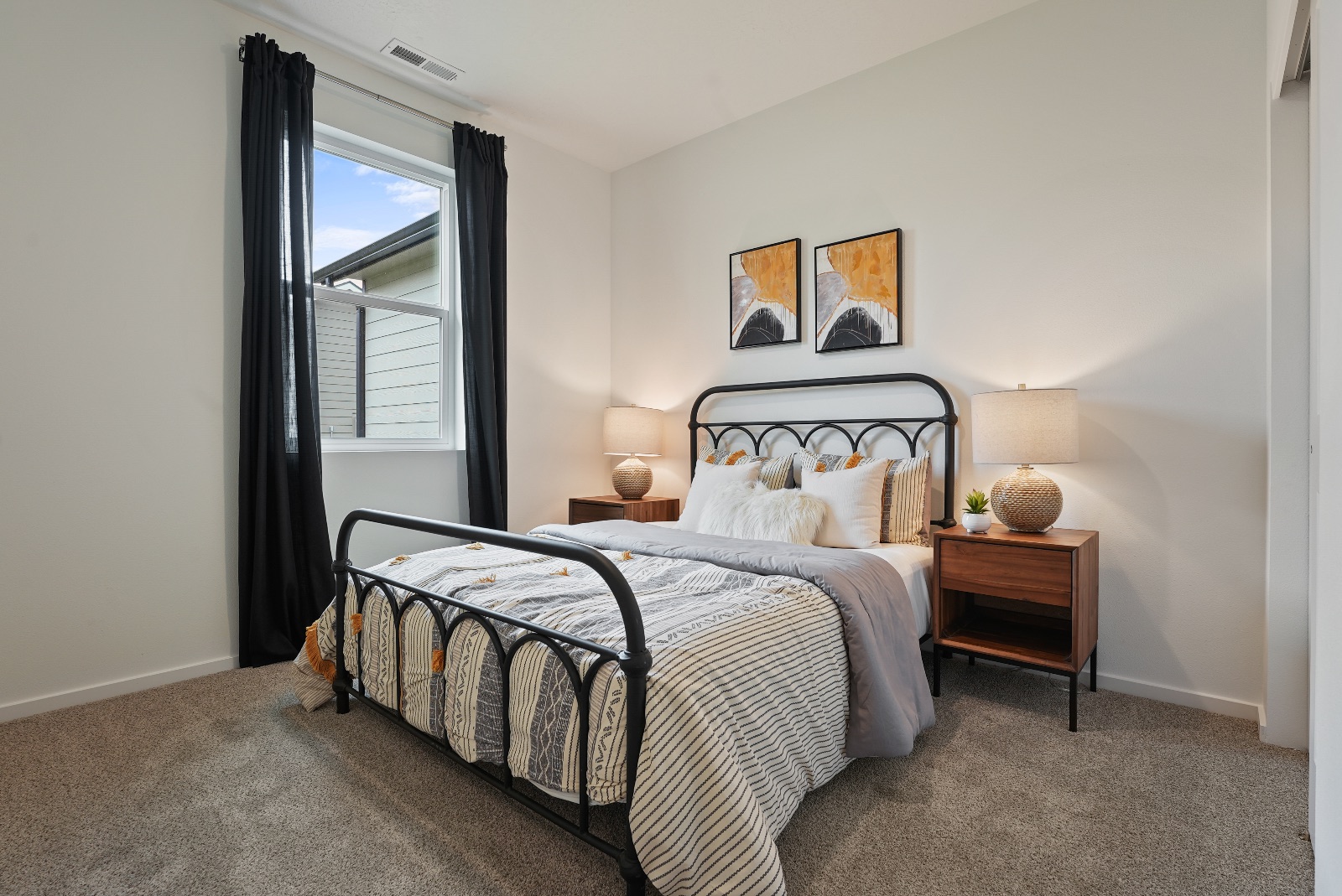 A secondary bedroom with a window onto the side yard, carpet, and a black metal bed frame.