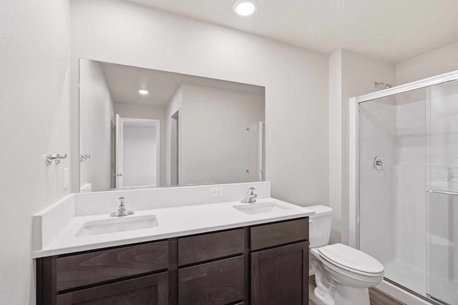 The kitchen in a Phoenix plan home: espresso shaker cabinetry, stainless appliances, and a long island in white solid surface with an undermount sink.