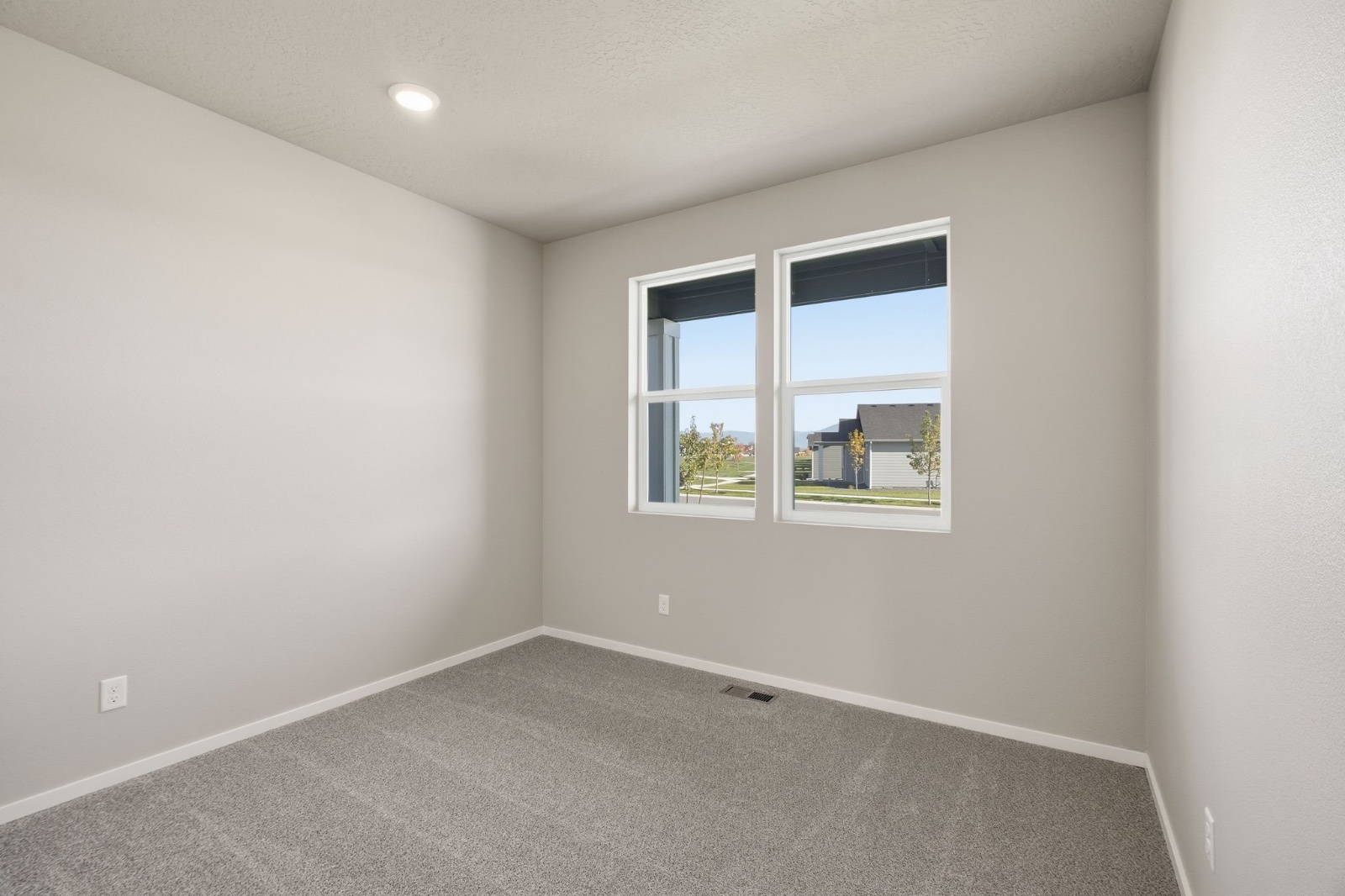 The carpeted primary bedroom in a Phoenix plan home, with paired windows over the neighborhood green.