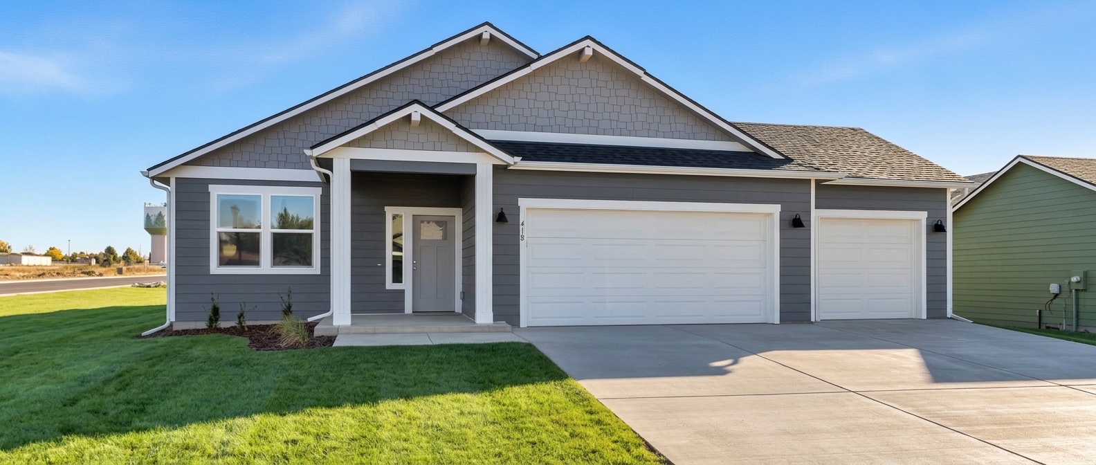 An Eagle plan home, not 409 N Washington Ave: a single-level craftsman in slate grey lap siding with shake gable accents, white trim, a covered entry porch, and a three-car garage — a double bay and a single bay.