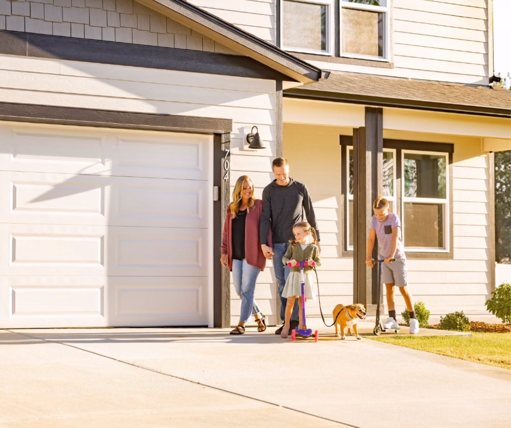 A family and their dog heading out of the house down the driveway.
