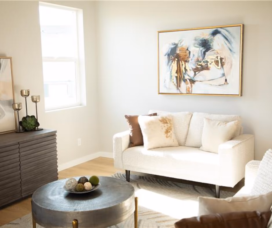 A sunlit living room with a cream sofa, framed artwork and a round coffee table.
