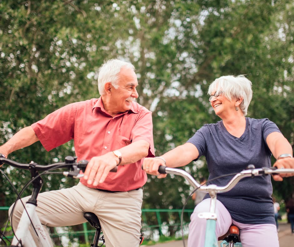 A couple riding bicycles side by side along a tree-lined path.