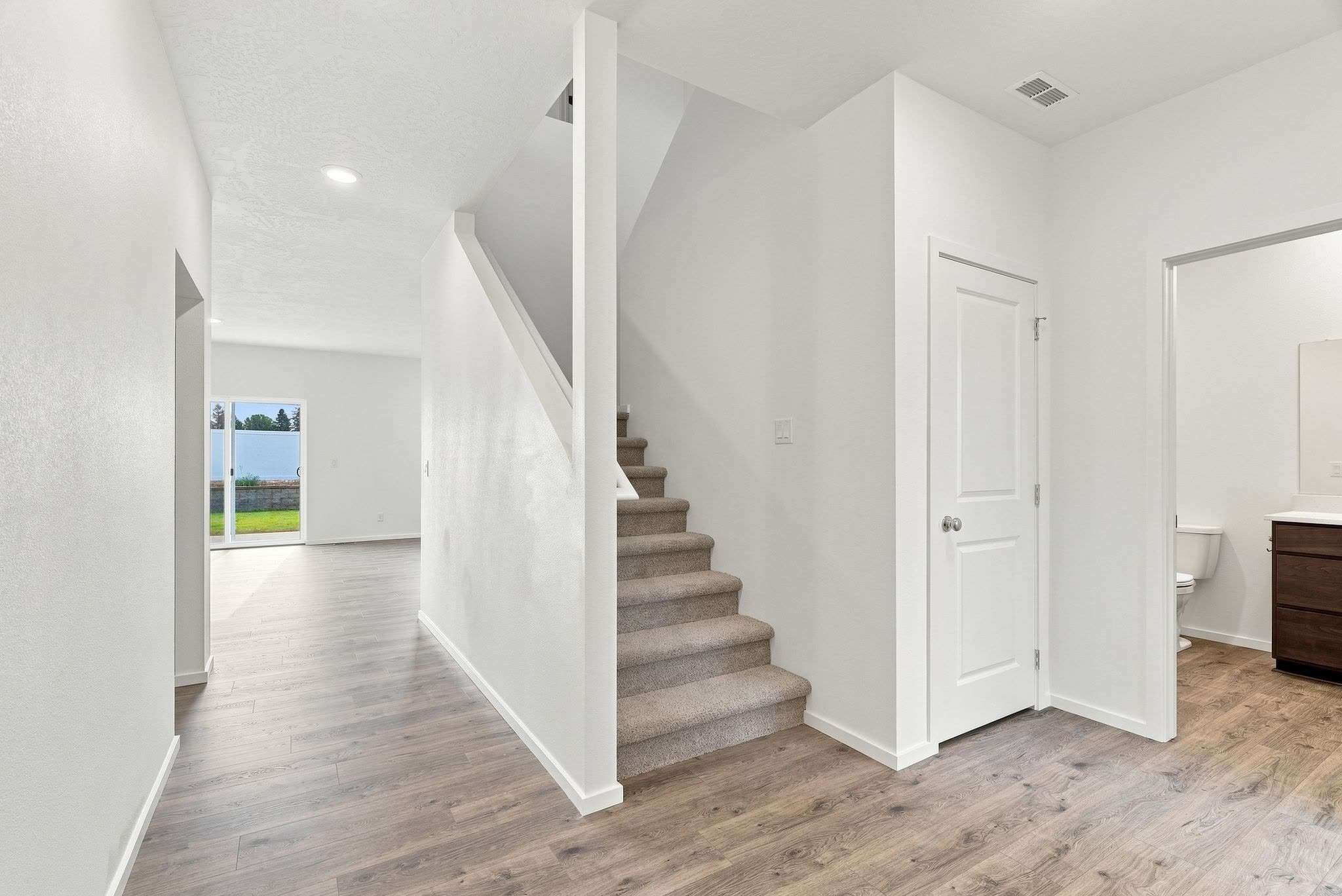A Clearwater plan entry in luxury plank flooring, looking through to the living room, with the carpeted stair to the second floor.