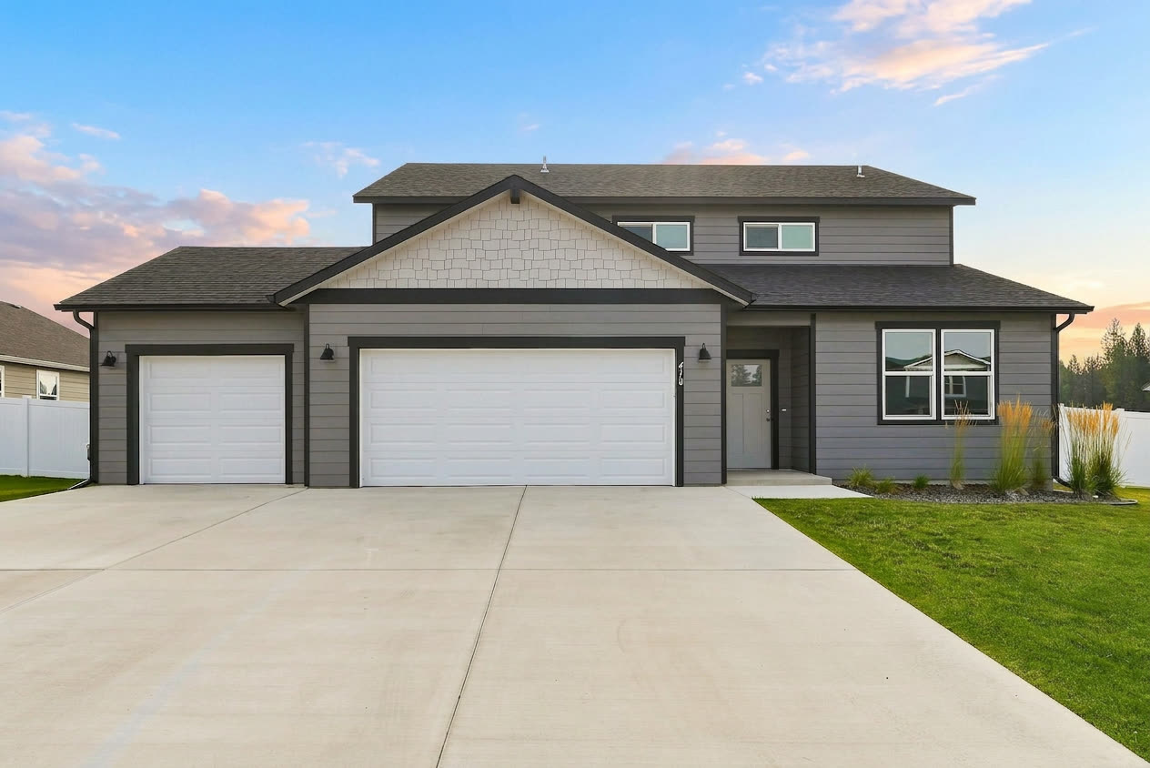 The front of 410 N Washington Avenue at dusk: two stories in gray lap siding with shake accents in the gable, charcoal trim, a covered entry, and a three-car garage off the wide driveway.