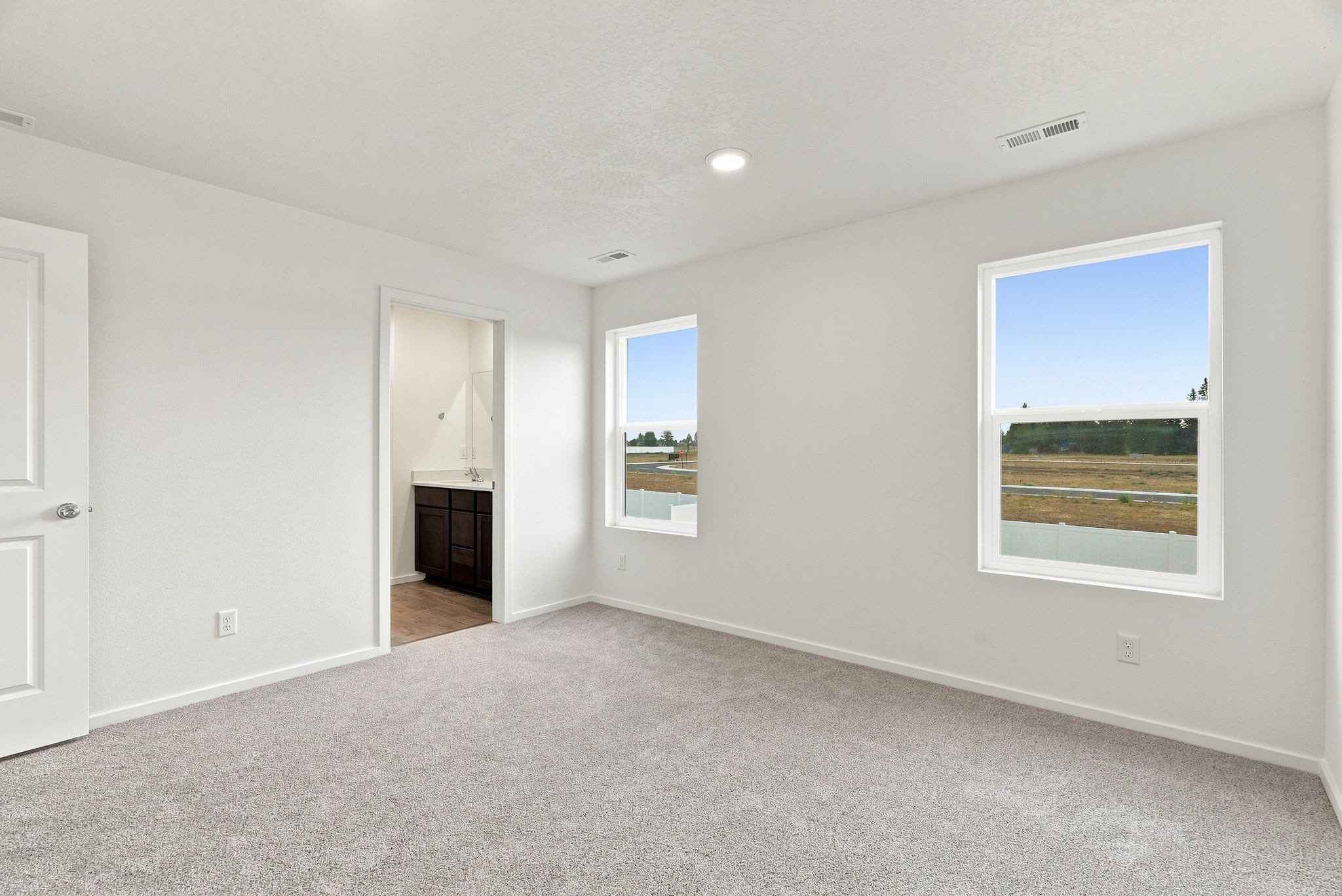A Clearwater plan primary bedroom, carpeted, with two windows and the ensuite bath beyond.