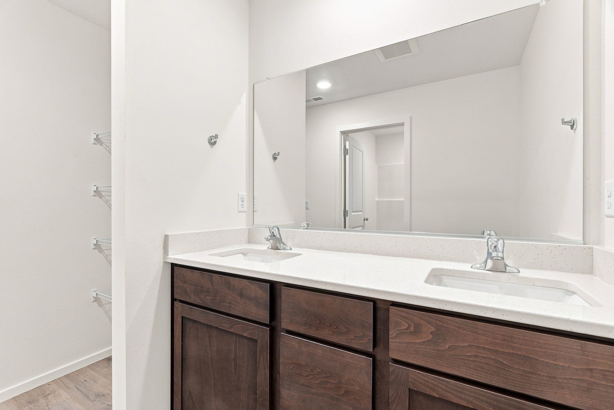 A Clearwater plan primary bath with a dual-sink quartz vanity under a full-width mirror, and the walk-in closet alongside.