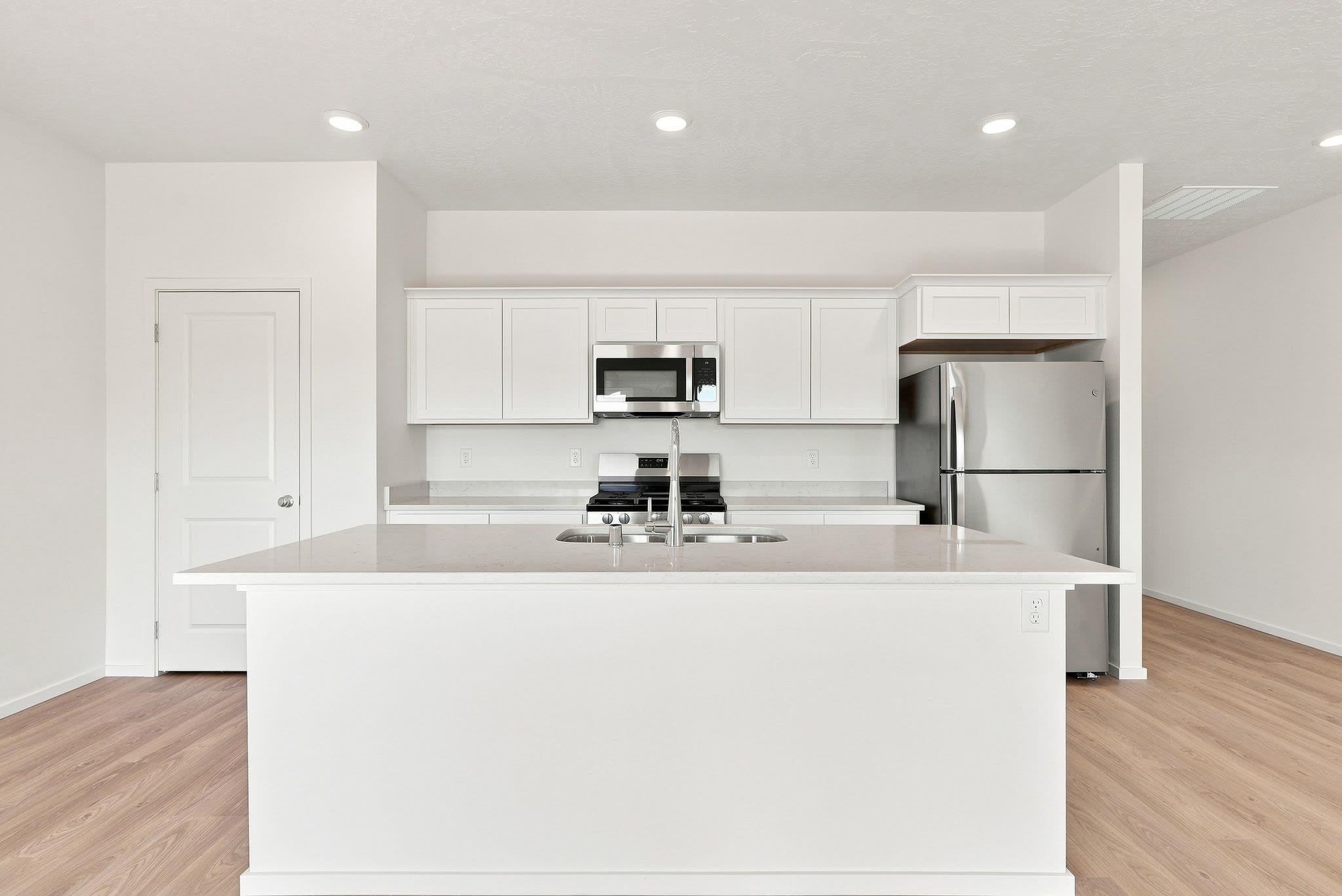 The kitchen island in quartz, with white shaker cabinetry, a stainless gas range, microwave and refrigerator behind.