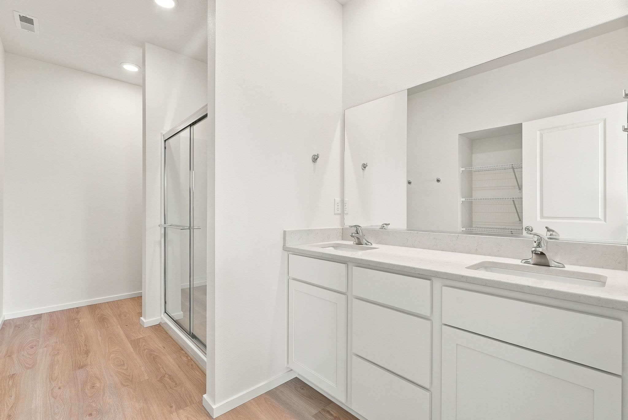 The primary bath: a dual-sink quartz vanity under a full-width mirror, a glass-enclosed shower, and the walk-in closet alongside.